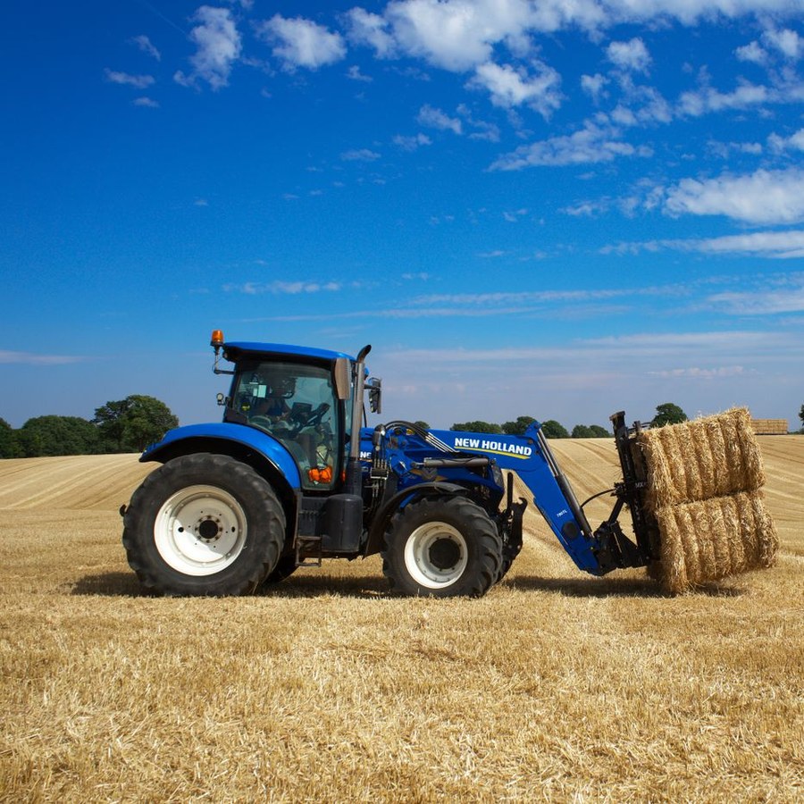 Tractor lifting hay bales in a harvested field